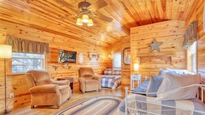 Ein gemütliches Blockhaus-Interieur mit einem Bett, zwei Sesseln, einem Sofa, einem Deckenventilator und einem großen Fenster.