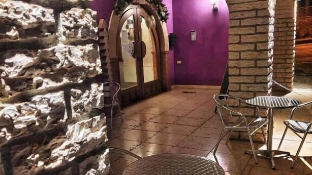 A stone-walled interior with a purple wall, a wooden door, and metal tables and chairs. - Hotel Piccola Mantova (Bosco Chiesanuova)