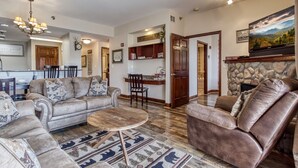 A spacious living room with a fireplace, a dining area, and a kitchen visible in the background. - Gorgeous 2BD/2BTH Condo w/ ∆ Views Pool Hot Tub Game Room 1/4 Mi to Parkway (Pigeon Forge)
