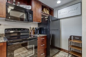 Cozinha equipada com micro-ondas, fogão, geladeira, armários de madeira e cafeteira.