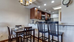 A dining area with a wooden table and chairs, a chandelier, and a kitchen in the background. - Gorgeous 2BD/2BTH Condo w/ ∆ Views Pool Hot Tub Game Room 1/4 Mi to Parkway (Pigeon Forge)