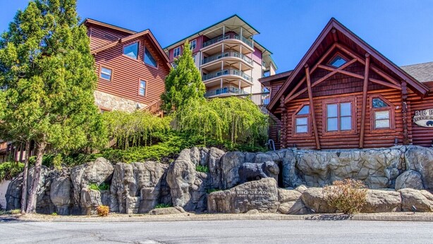 A lodge with a stone facade, wooden cabins, and a clear sky. - Gorgeous 2BD/2BTH Condo w/ ∆ Views Pool Hot Tub Game Room 1/4 Mi to Parkway (Pigeon Forge)