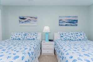 A bedroom with two beds, each with a blue patterned bedspread, a nightstand with a lamp, and two wall-mounted paintings. - 127th Bayside-pool-short walk 2 beach-By Park! (Ocean City)