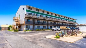 A multi-story motel with a parking lot, bicycles, and a vehicle parked in front. - 127th Bayside-pool-short walk 2 beach-By Park! (Ocean City)