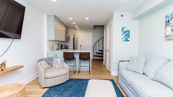 A living room with a sofa, ottoman, and a blue rug. There is a kitchen area with a dining table and chairs.