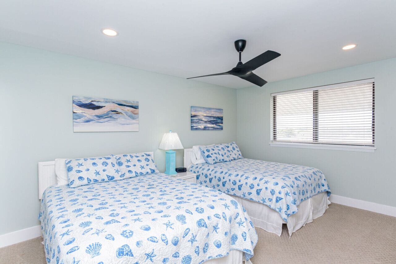 A bedroom with two beds, a ceiling fan, and artwork on the walls.