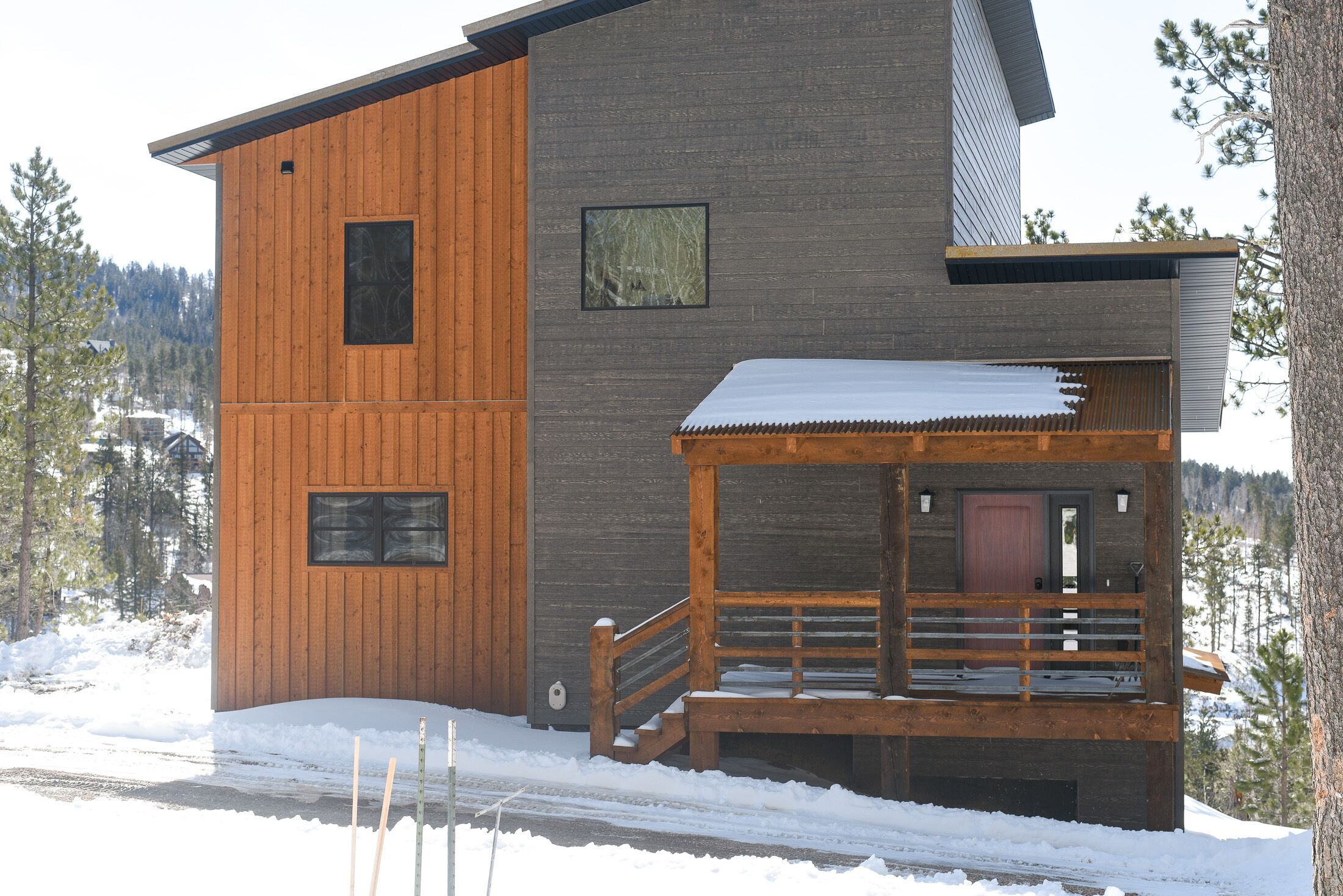 A modern cabin with a wooden exterior and a balcony, surrounded by snow and trees.