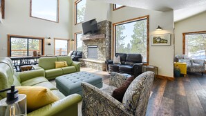 A spacious living room with a stone fireplace, large windows, and comfortable seating. - New 3-Level Lodge w/ Amazing View Close to Slopes & Trails w/ Great Amenities (Lead)