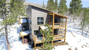 Una cabaña de varios pisos con un balcón de madera, rodeada de árboles y nieve.
