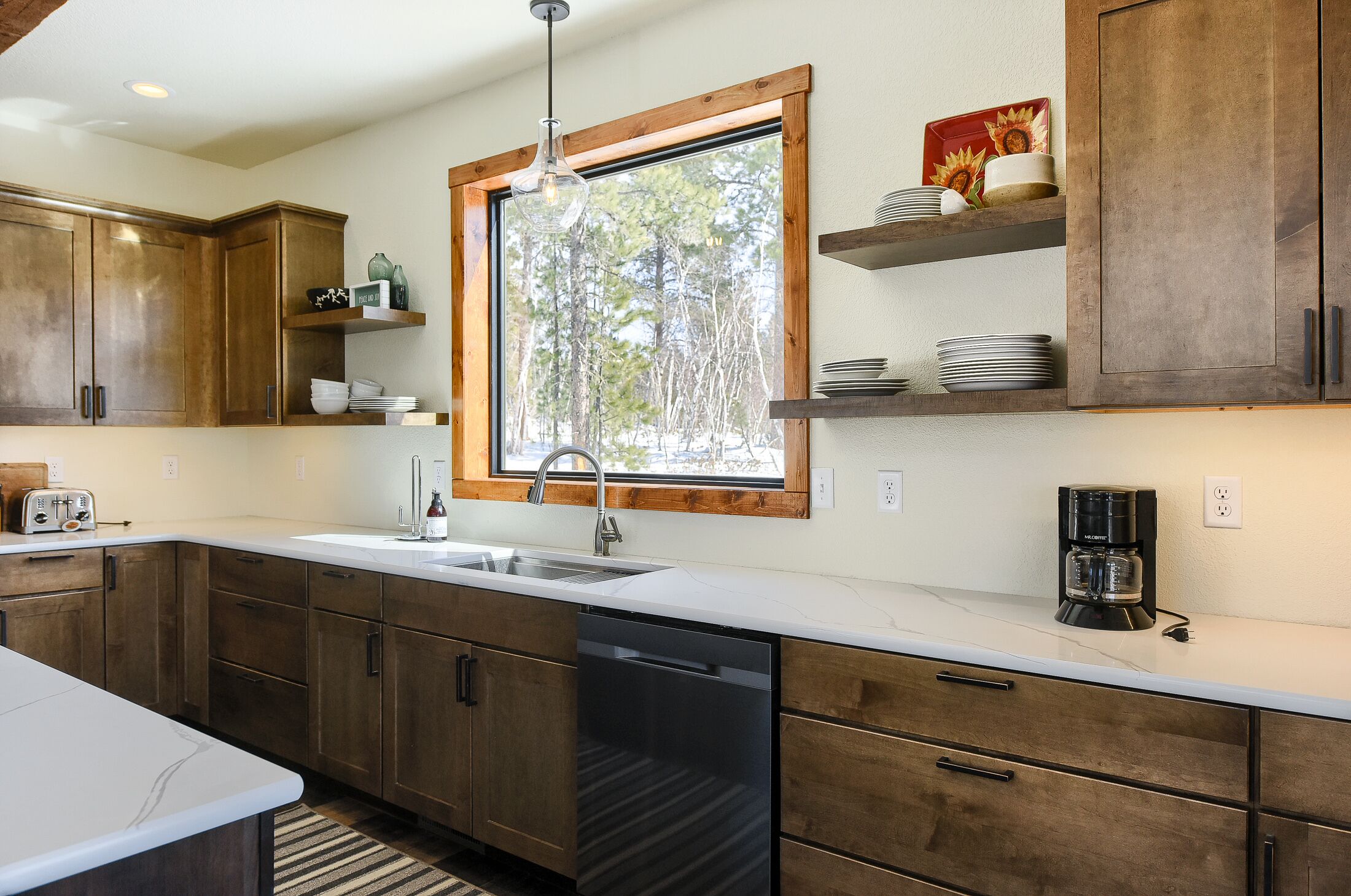 A modern kitchen with wooden cabinets, a large window, and a coffee maker on the countertop.