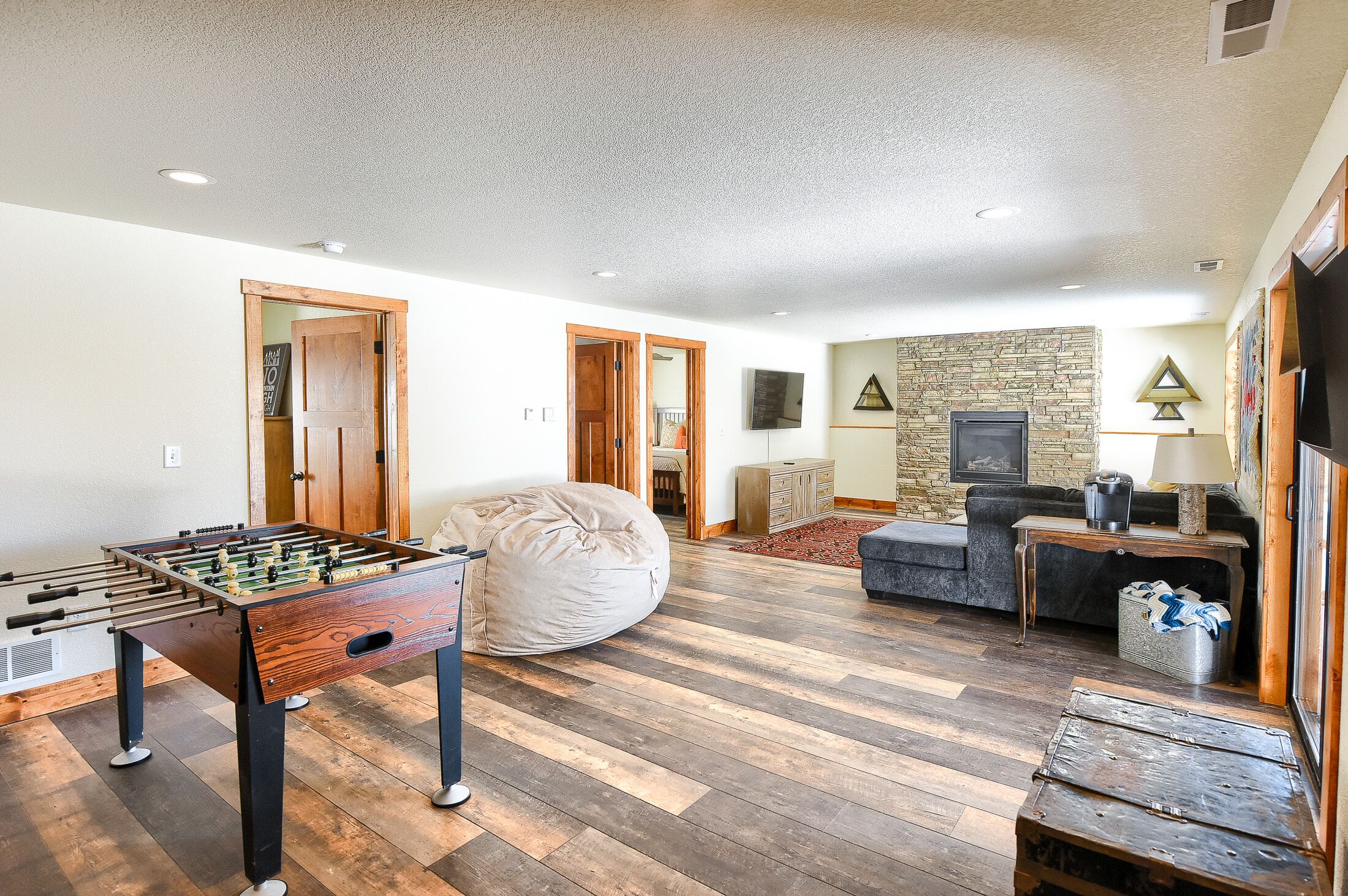 A spacious living room with a foosball table, a bean bag, a sofa, and a stone fireplace.