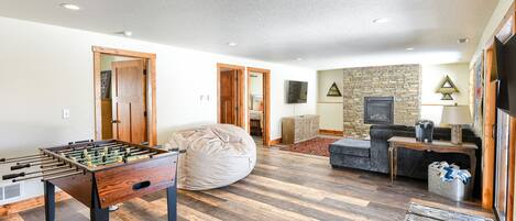 A spacious living room with a foosball table, a bean bag, a sofa, and a stone fireplace.