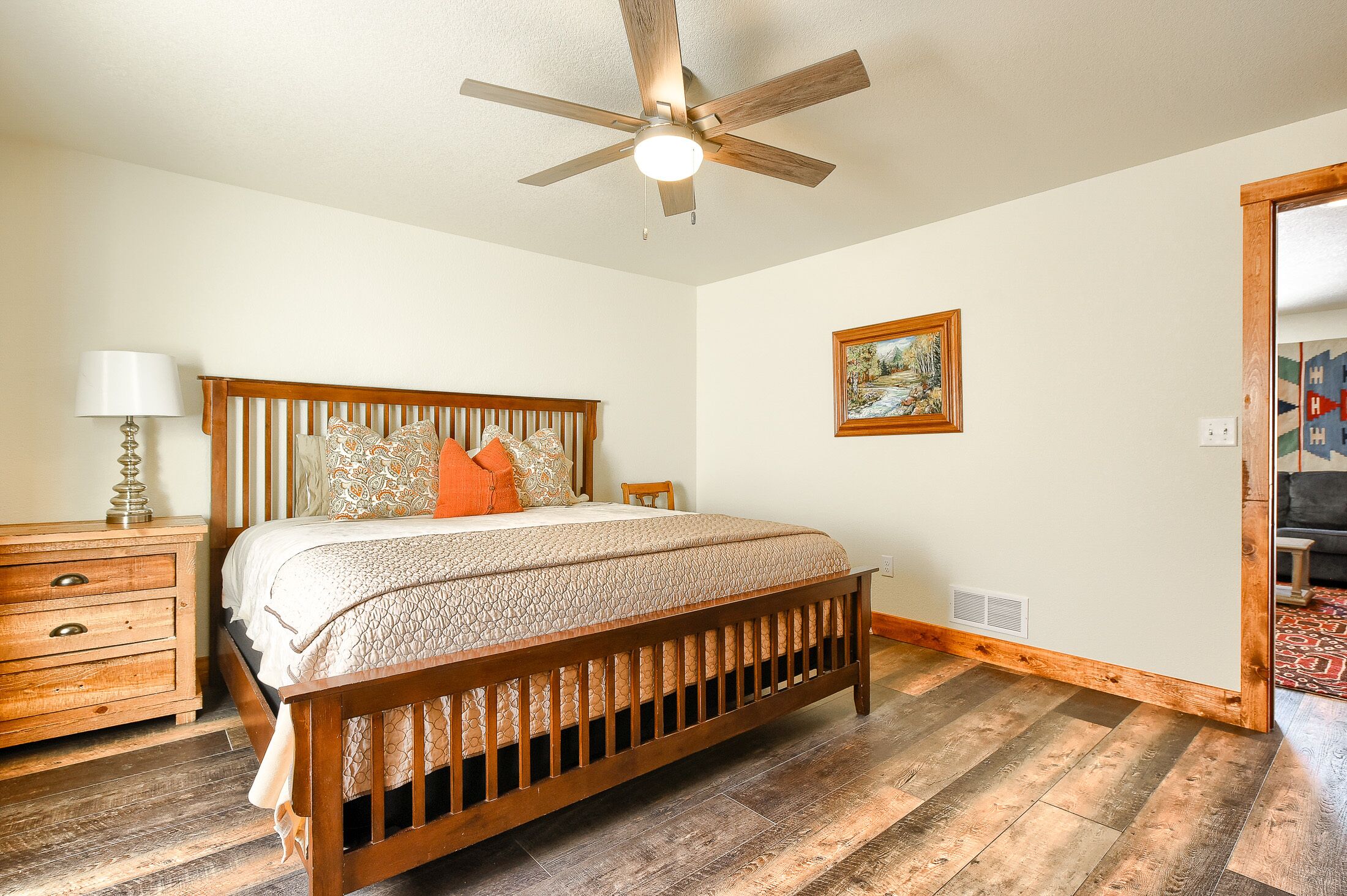 A bedroom with a wooden bed, a nightstand, a lamp, and a ceiling fan.
