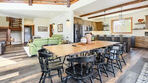 A spacious dining area with a wooden table and black chairs, a kitchen with modern appliances, and a lofted wooden staircase. - New 3-Level Lodge w/ Amazing View Close to Slopes & Trails w/ Great Amenities (Lead)