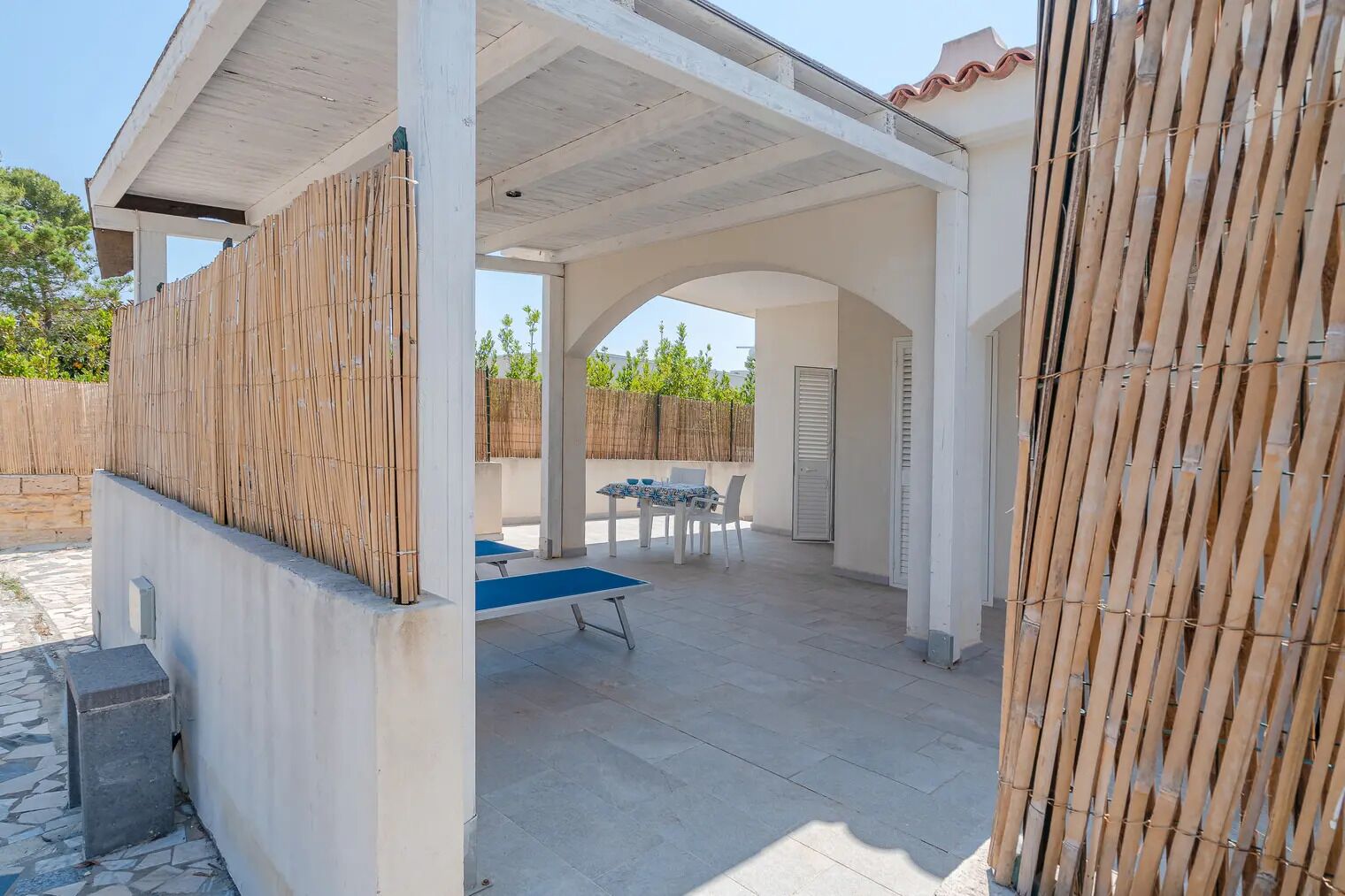 Un espace extérieur aménagé avec une table et des chaises, un coin salon abrité et une clôture en bambou.