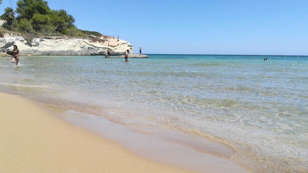 A beach with clear shallow waters, a sandy shore, and rocky cliffs in the background. - THE STACKS 3 (Lido di Noto)