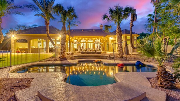 Una casa lujosa con piscina, palmeras y un patio bien iluminado.