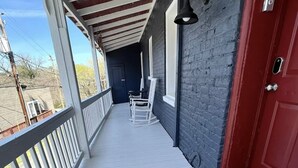 Un porche abrité avec une balustrade blanche, une porte rouge et un paillasson.