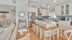 Una cocina moderna con armarios blancos, una isla central con taburetes de bar, electrodomésticos de acero inoxidable e iluminación colgante.