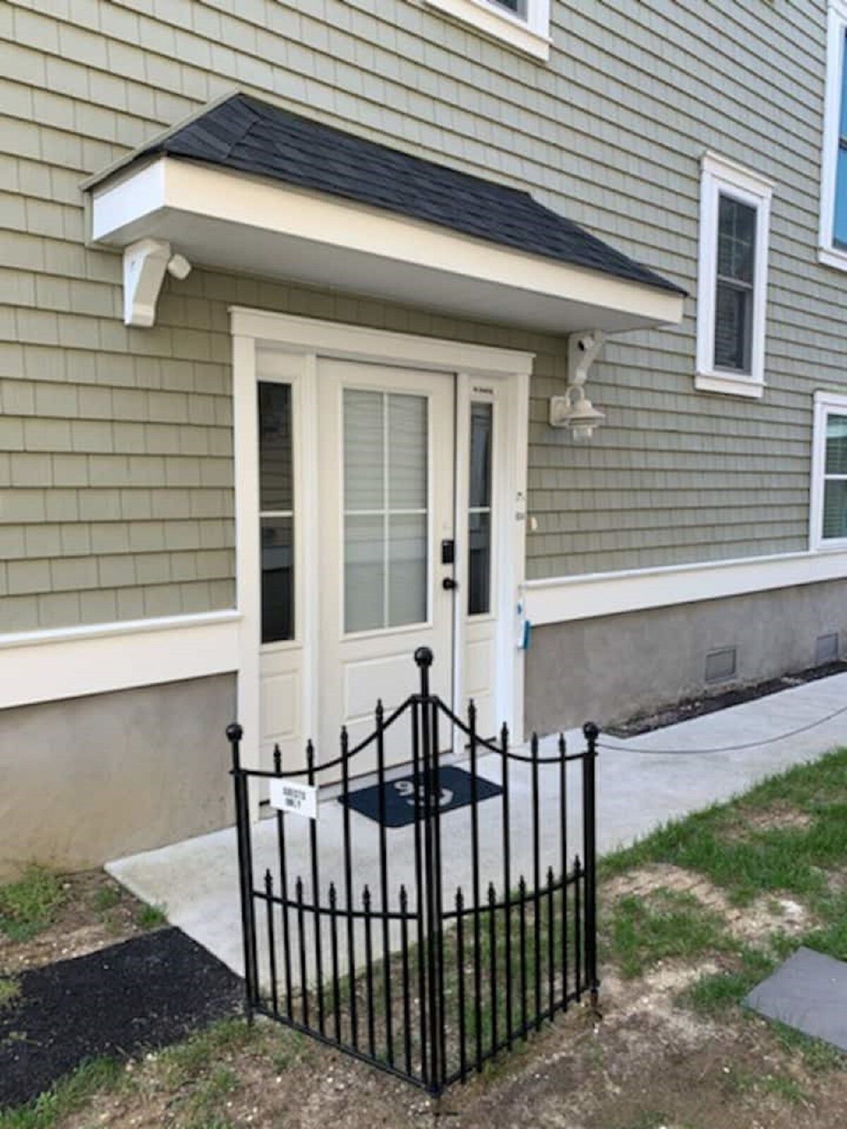 A residential building with a gated entrance, a covered porch, and a small front yard.