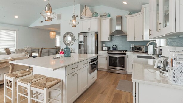 Una cocina moderna con armarios blancos, electrodomésticos de acero inoxidable y una isla central con taburetes de bar.