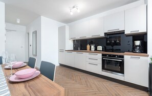Uma cozinha moderna com armários brancos, bancada de madeira e piso em padrão herringbone.