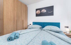 Quarto com cama, mesa de cabeceira, luminária e uma obra de arte na parede.