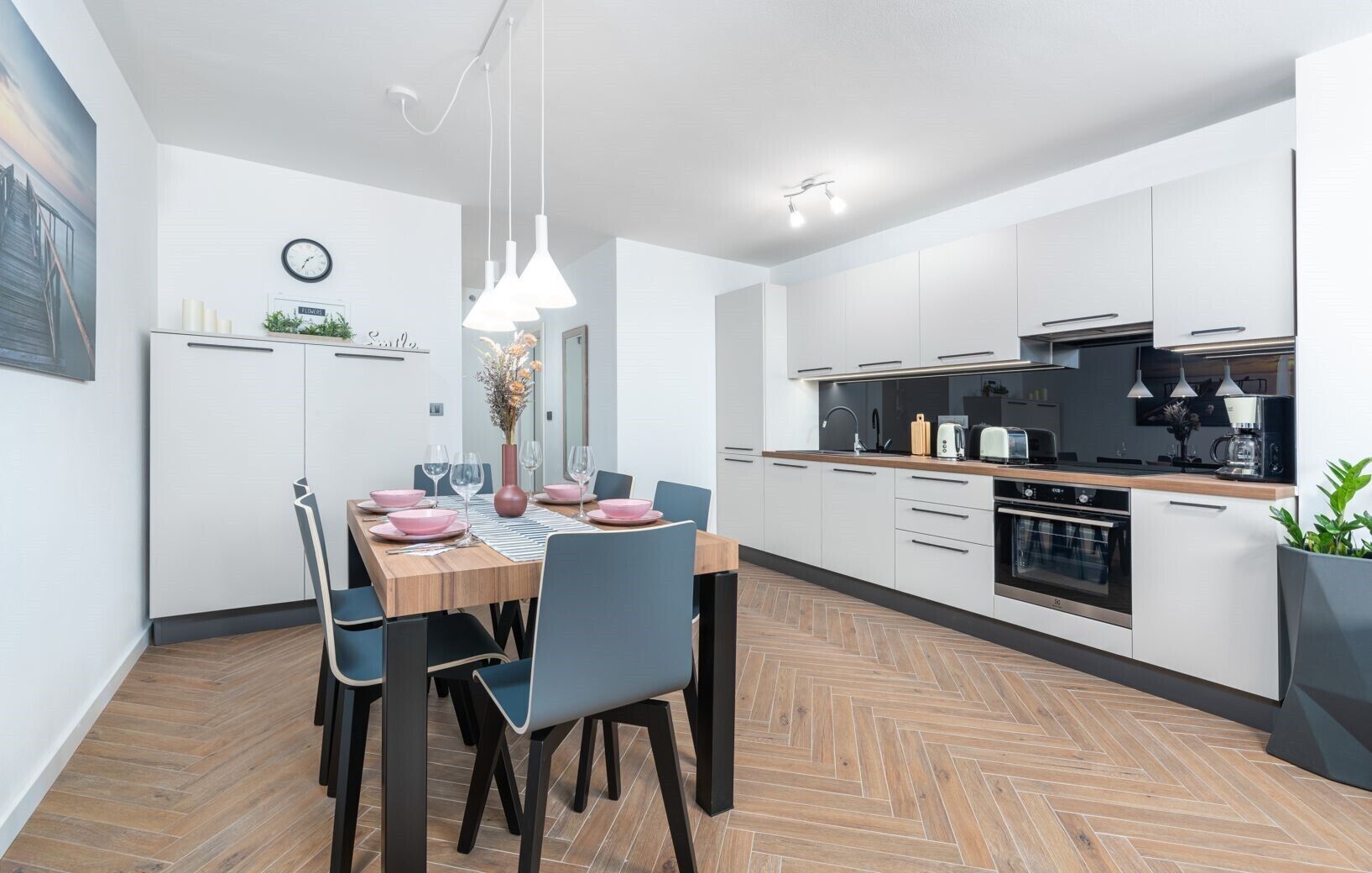 A modern kitchen with white cabinets, a wooden countertop, and a dining area with a table set for four.
