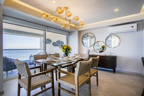 Un coin repas avec une table en verre, des chaises en osier et une vue sur l’océan.
