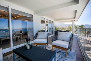 A balcony with two chairs, a table, and a view of the sea and cityscape.