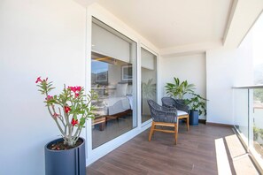 En moderne balkon med en glasdør der fører til et soveværelse, trægulv og potteplanter.