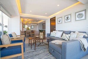 A modern living room with a sofa, chairs, a dining table, and a kitchen area in the background.