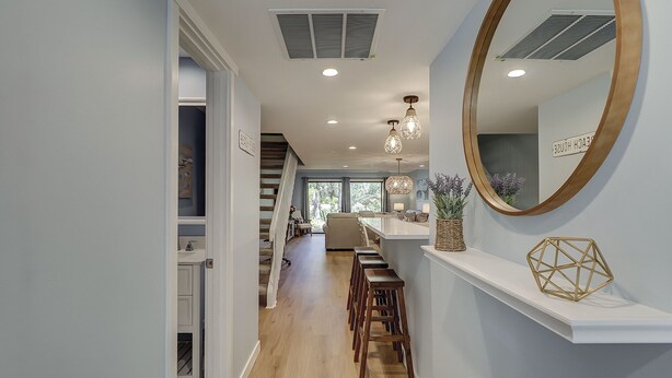 A hallway with a wooden floor, a white staircase, and a kitchen area with a bar. - Sunset Rentals | Shipmaster 1203 (Hilton Head Island)