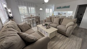 Una sala de estar con dos sofás color beige, una mesa de centro y un comedor con mesa y sillas.