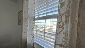 Una habitación con una ventana cubierta por cortinas estampadas, un cuadro en la pared y vistas de un edificio.