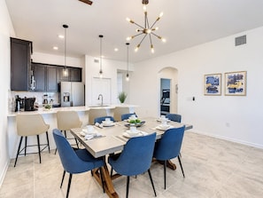 A modern kitchen with dark cabinets, a central island, and a dining area with blue chairs and a wooden table.