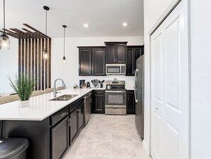 A modern kitchen with dark cabinetry, stainless steel appliances, and a white countertop.
