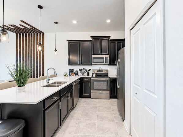 A modern kitchen with dark cabinetry, stainless steel appliances, and a white countertop.