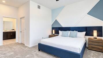 Quarto com cama, mesas de cabeceira, ventoinha no teto e banheiro visível através de uma porta aberta.