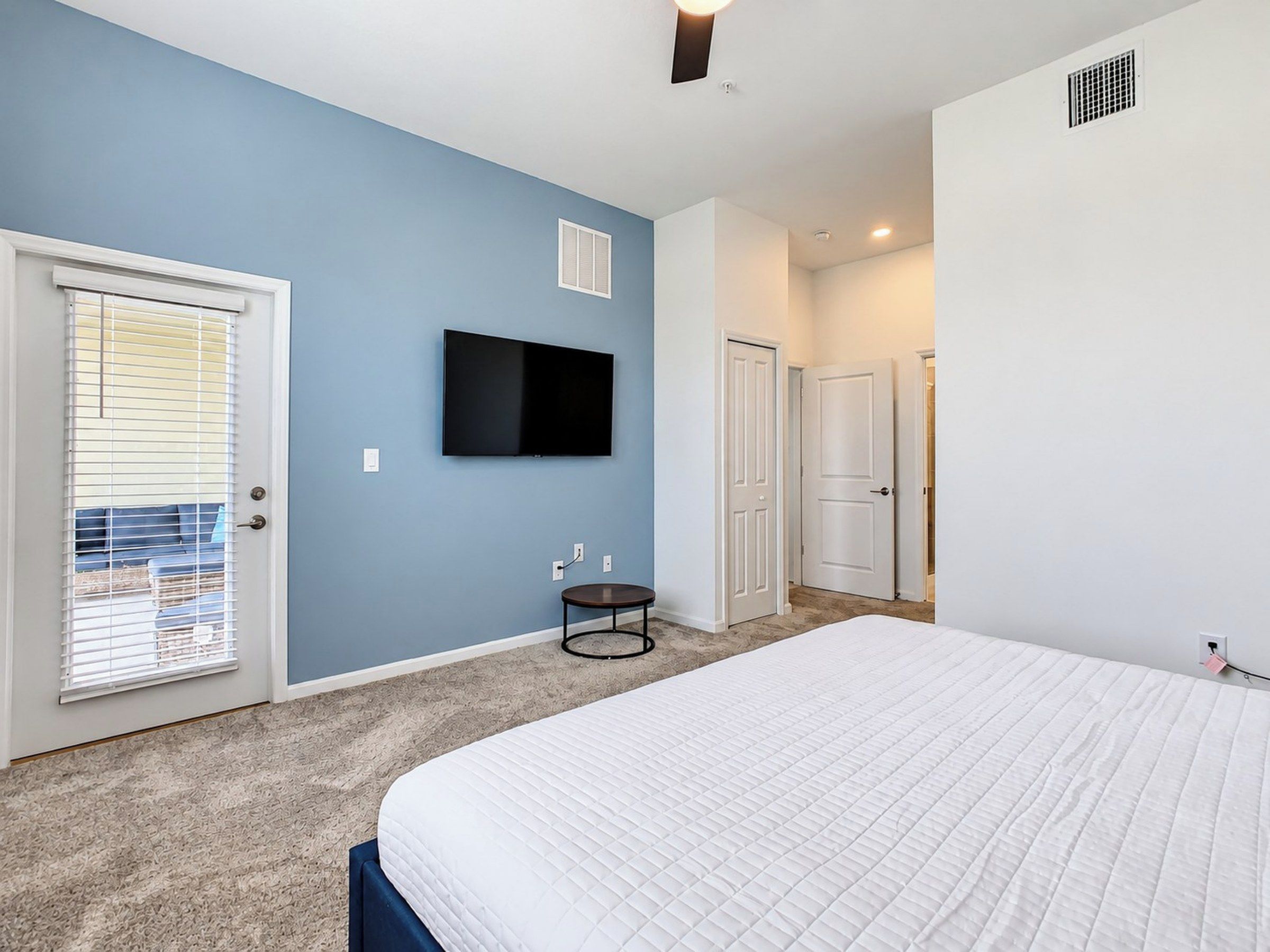 Quarto com cama grande, televisão na parede, porta com janela e piso coberto de carpete.