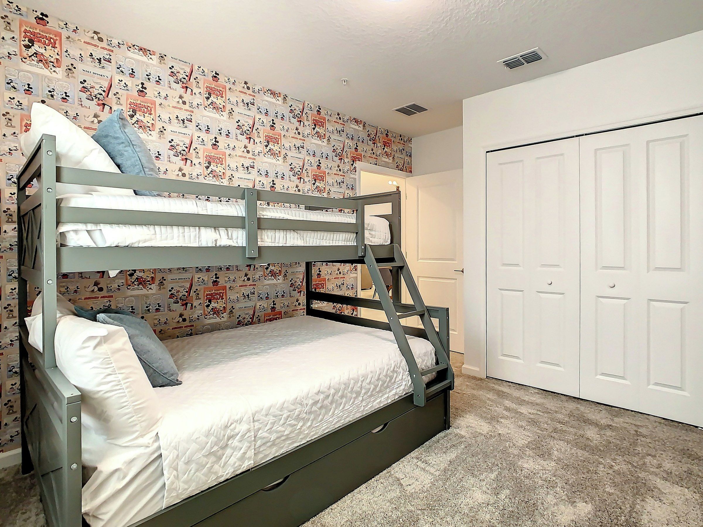 Uma cama beliche com uma cama inferior e uma gaveta extraível, uma porta branca e uma parede com papel de parede temático do Mickey Mouse.