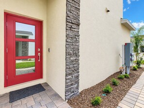 A red door with a glass panel, a stone accent wall, and a power box on the side.