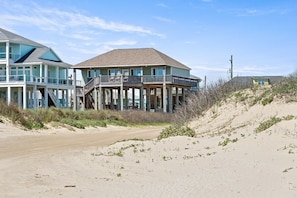 A beachfront house with a balcony, a covered porch, and a sandy beach in the background. - Beaches Be Trippin' 4 Bedroom Home by RedAwning (Port Bolivar)