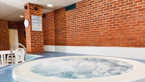 A hot tub in a room with a brick wall, a clock, and a white chair. - 48 The Bay (St Margarets at Cliffe,)