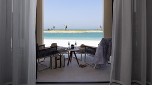 A balcony with a view of the beach, a table with a hat and a bag, and a pair of slippers on the floor. - Jumeirah Gulf of Bahrain (Zallaq)