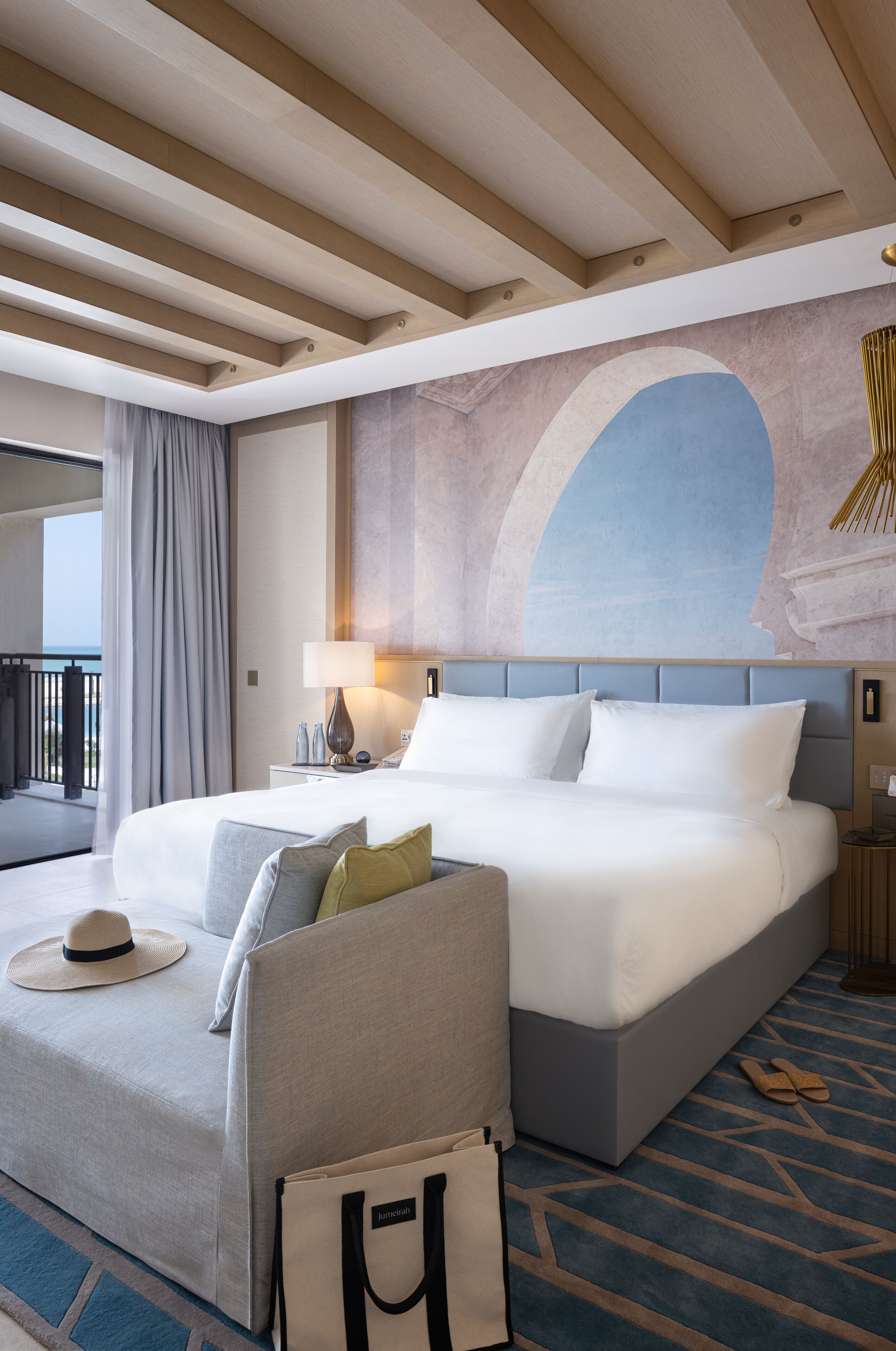 Habitación de hotel con una cama grande, un sofá, una mesita de noche, una lámpara y vistas al balcón.