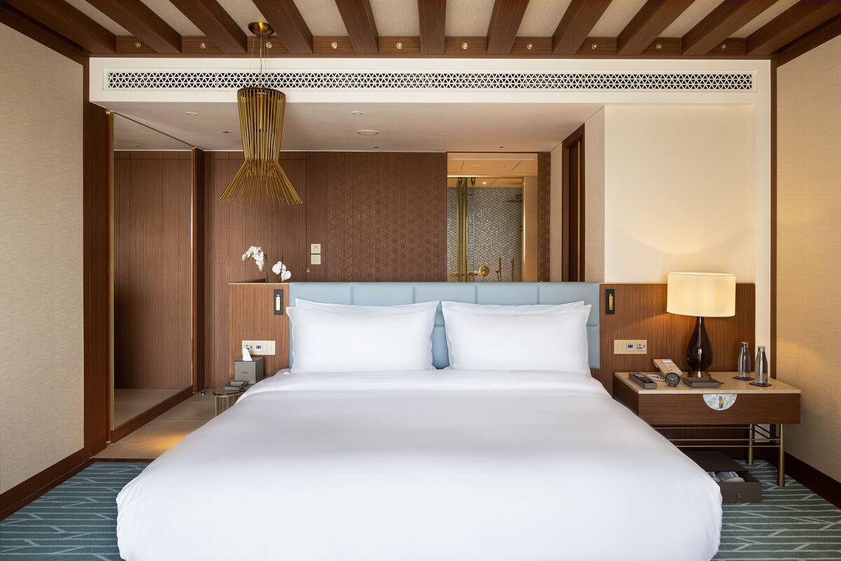 A large bed with a blue headboard, a bedside lamp, a nightstand, and a mirror.