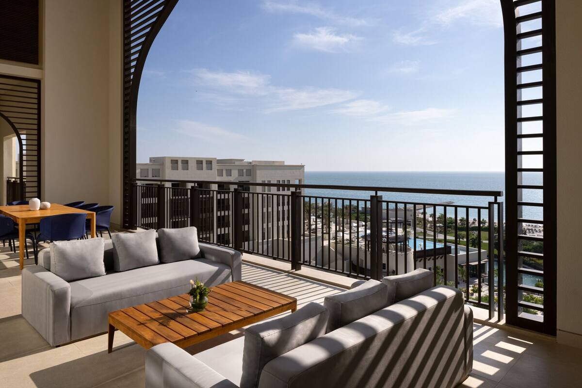 A balcony with a view of the sea, furnished with a sofa, chairs, and a coffee table.