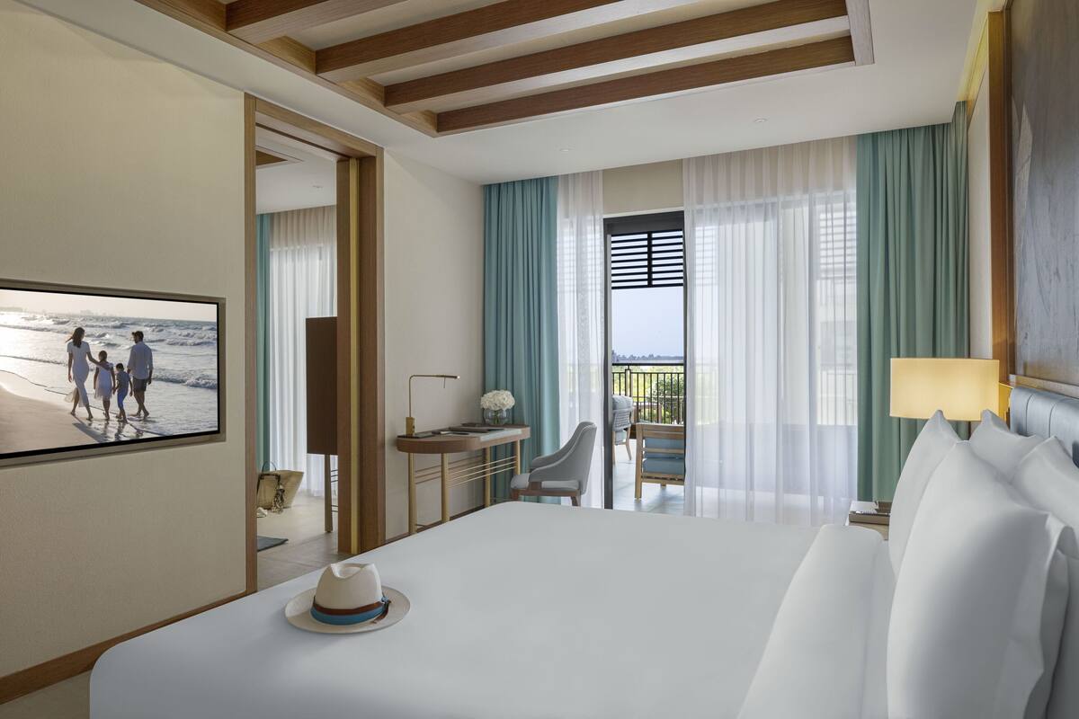 A hotel room with a large bed, a desk with a lamp, a chair, and a view of the ocean through the window.