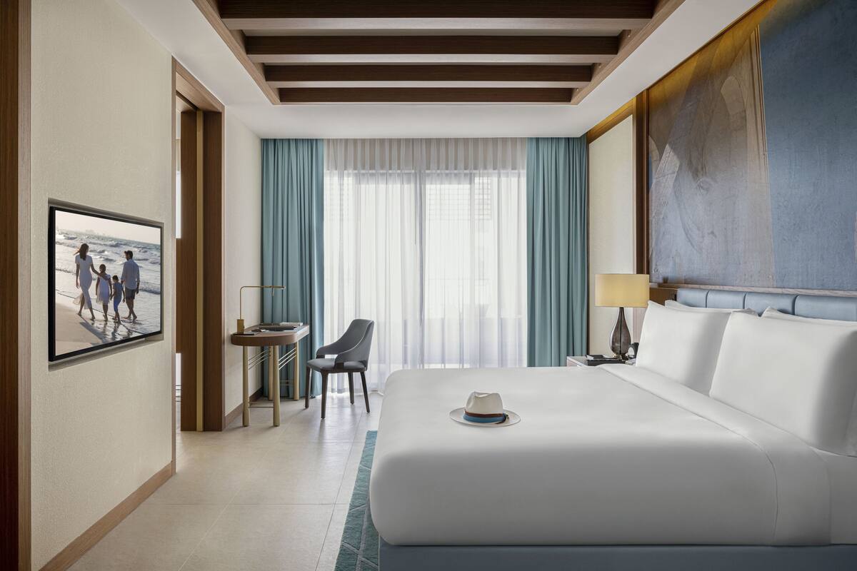 A hotel room with a large bed, a desk, a chair, a TV, and a painting on the wall.